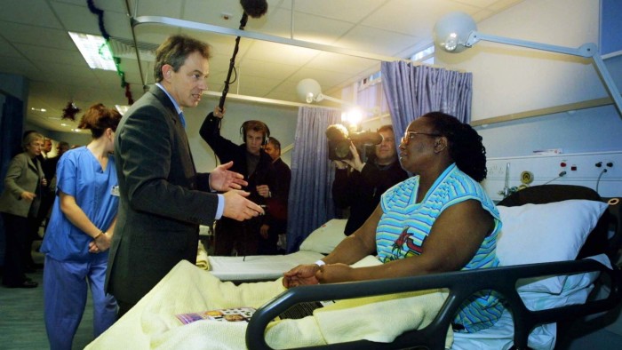 Tony Blair talks to a patient sitting in a hospital bed