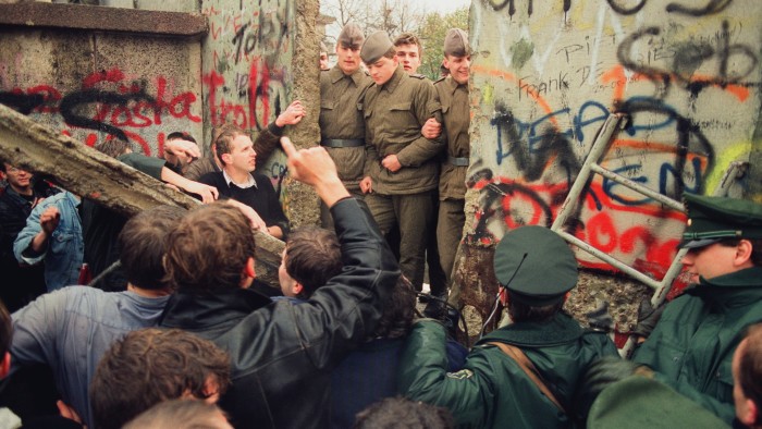 A group of West German demonstrators tear down a section of the Berlin Wall under the gaze of East-German border guards