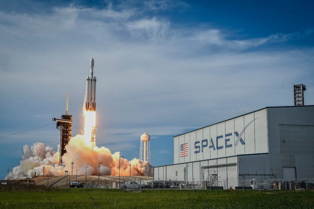 SpaceX rocket taking off from a launch site, in foreground SpaceX on a building.