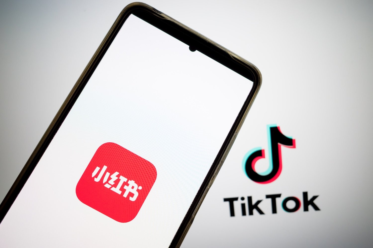 The RedNote logo appears on a smartphone screen, and the TikTok logo appears on a computer screen as the background in this photo illustration.