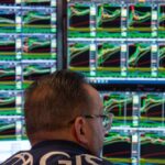 A trader on the New York Stock Exchange floor is focused on multiple screens displaying colourful stock charts and data.