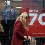 A woman walks past a store window advertising up to 70% off items