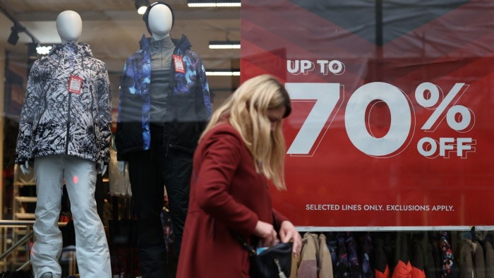 A woman walks past a store window advertising up to 70% off items