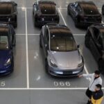 Tesla electric vehicles are parked in a delivery centre in Beijing. Two people walk past the cars