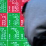 A man walk past an electronic board showing stock prices in Tokyo