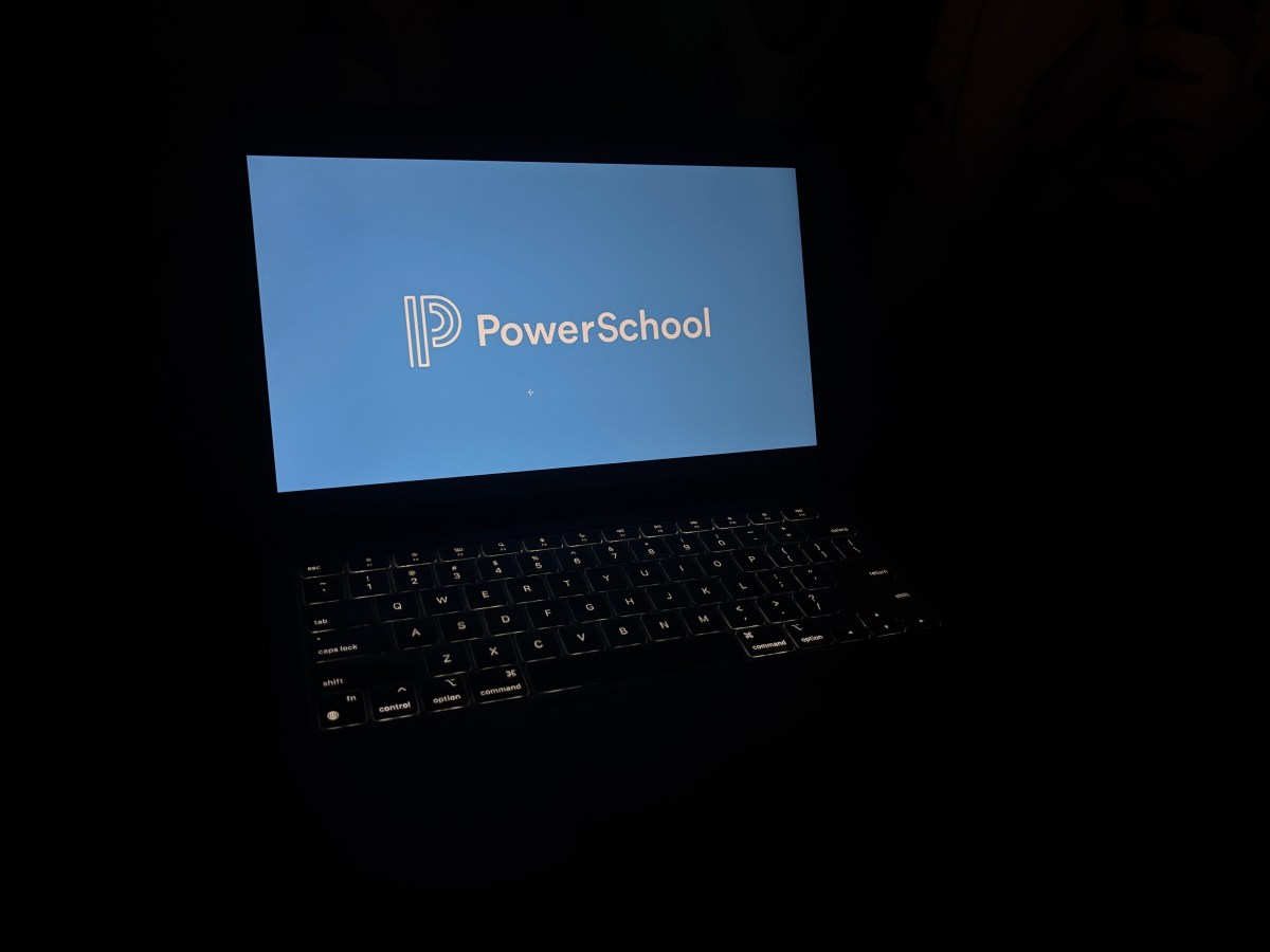 a laptop in a dark room with the laptop keyboard lit up, and the display reads PowerSchool with its corporate logo.