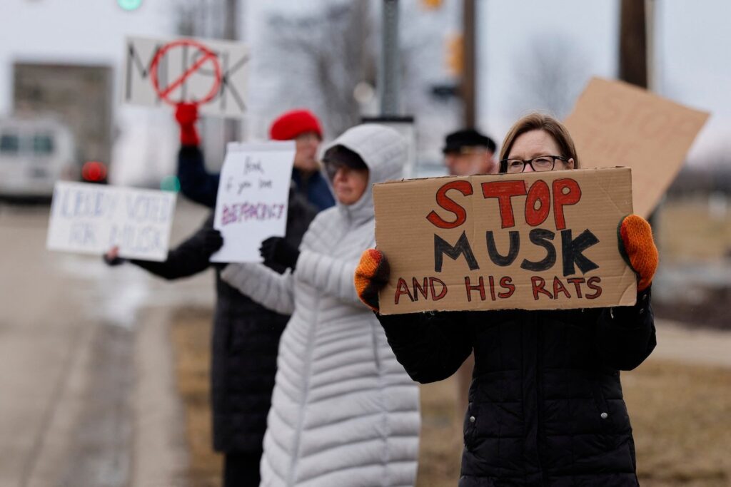 People hold signs during a protest against Elon Musk outside of a Tesla dealership in West Bloomfield, Michigan, on February 27, 2025