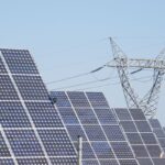 Solar panels stand in front of a high-voltage power line.