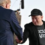 Elon Musk shaking the hand of Donald Trump in the foreground, back to the camera.