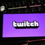 Twitch logo appears on a phone screen that sits above an illuminated keyboard.