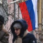 People walk past Russian and US flags hanging on the main building of the US Embassy in Moscow