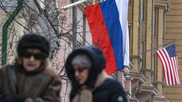 People walk past Russian and US flags hanging on the main building of the US Embassy in Moscow