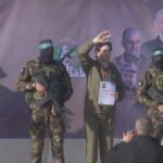 Masked Hamas gunmen stand on a platform with a hostage, who is waving