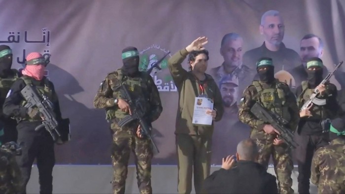 Masked Hamas gunmen stand on a platform with a hostage, who is waving