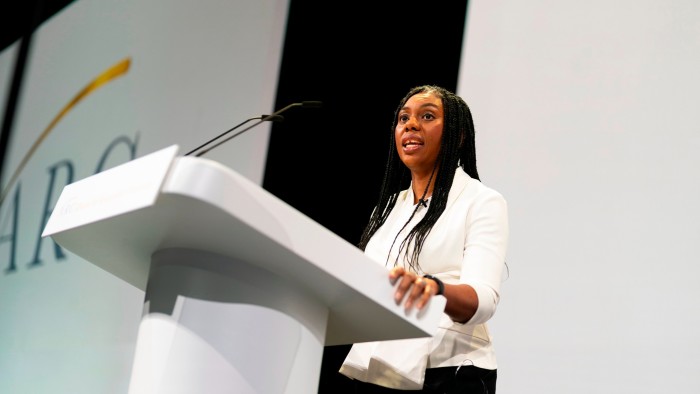 A woman in a white top stands at a large white podium talking