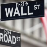 A Wall Street sign hangs in front of a US flag outside the New York Stock Exchange