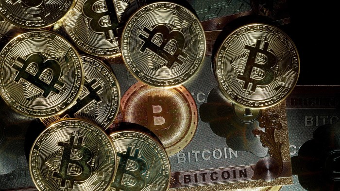 Gold-coloured coins with the bitcoin symbol are arranged on a dark surface