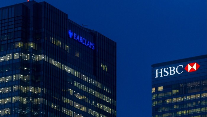 Barclays and HSBC headquarters in London, England, illuminated at night with their logos glowing against a dark blue sky