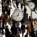 People walking in the street. There are number of clocks on metal poles