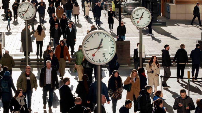 People walking in the street. There are number of clocks on metal poles