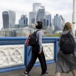 Commuters cross Tower Bridge with skyscrapers in the City of London in the background