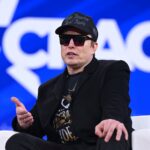 Elon Musk on stage at CPAC in Maryland with sunglasses on and a MAGA hat