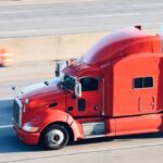 A red semi towing a trailer drives down a highway.