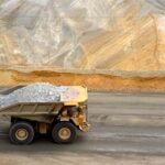 A large yellow dump truck carries ore out of a pit mine.