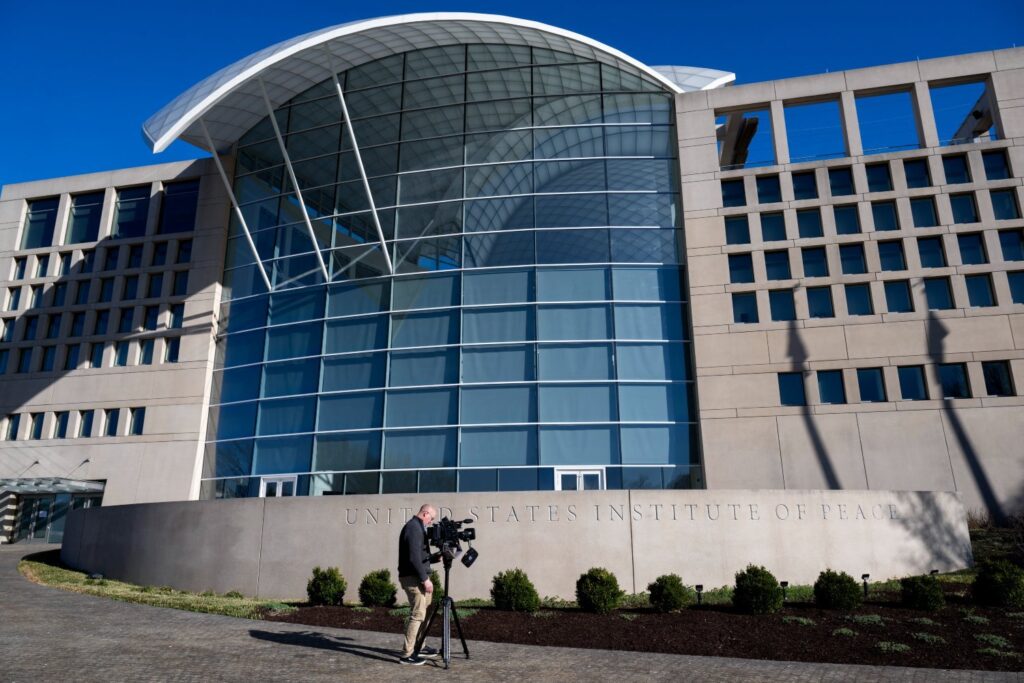 A journalist with a video camera pointed at the exterior of the US Institute of Peace building