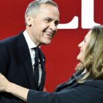 Mark Carney and Chrystia Freeland shake hands and smile warmly at each other against a red background