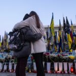 Two people embrace with their backs to the camera in front of memorial to the Ukrainian war dead