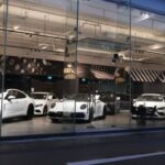 White cars are displayed in a well-lit, modern glass-front Vincar showroom