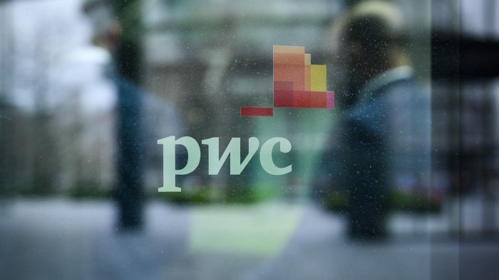 People walk past a sign on a window on the exterior of the PWC London offices