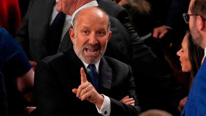 Howard Lutnick gestures with his hand as he interacts with others in a crowded setting before Donald Trump's address to Congress