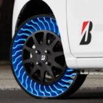 A close-up of Bridgestone’s prototype airless tyre on a white vehicle. The tyre features a unique blue and black design with an open lattice structure