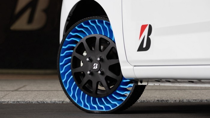 A close-up of Bridgestone’s prototype airless tyre on a white vehicle. The tyre features a unique blue and black design with an open lattice structure