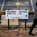 People walking past a city of Westminster road sign showing Parliament street to the left and Whitehall to the right