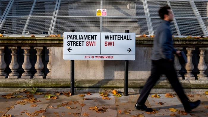 People walking past a city of Westminster road sign showing Parliament street to the left and Whitehall to the right