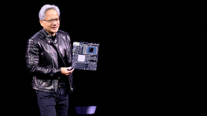 Jensen Huang holds up a circuit board while delivering a speech in a black leather jacket and standing against a dark background