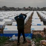 A boy stands on a hill, looking over a large tent camp for displaced Palestinians