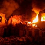 Flames and thick smoke engulf a building in Krasnopillia, Sumy region, Ukraine on March 19 2025. The structure is heavily damaged, with fire visible through the windows and debris scattered in the foreground.