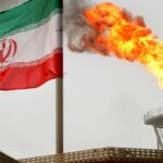 A gas flare on an oil production platform alongside an Iranian flag