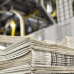 stack of freshly printed daily newspapers transported to a printing plant, in the background machines and technical equipment of a large printing plant